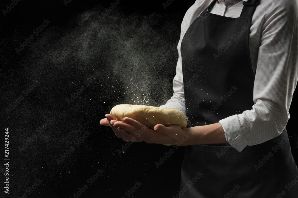 Dough in the hands of the chef's chief with flour on a dark background. The concept of cooking food, pizza, sweets, pastas, bread and bakery products