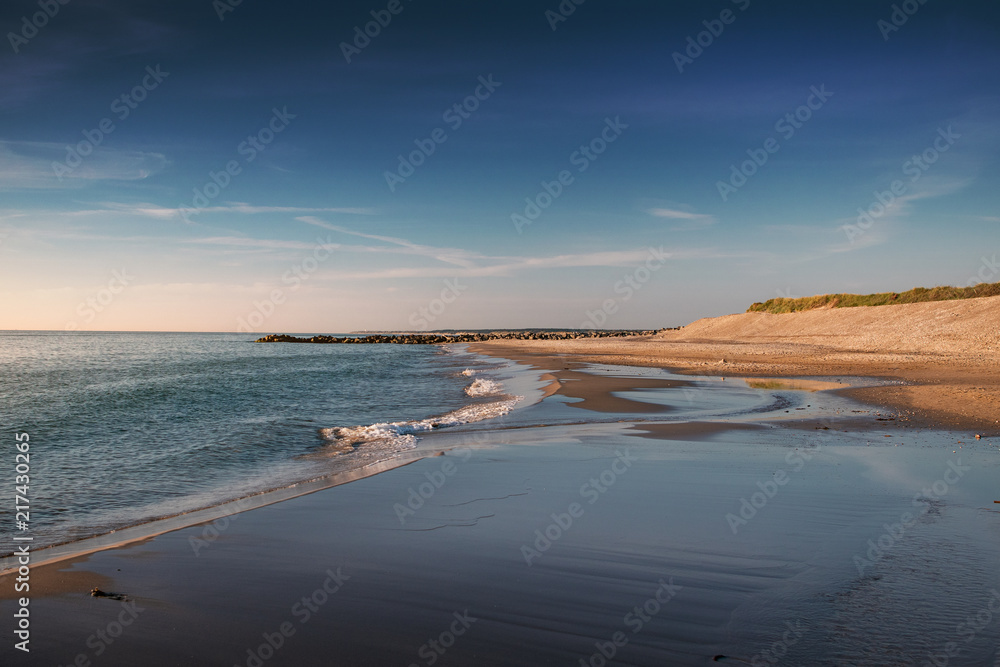 Evening seascape beach scene with waves and blue sky and yellow sand dunes