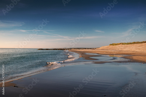 Evening seascape beach scene with waves and blue sky and yellow sand dunes