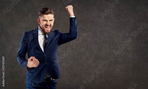 A young businessman with a beard enjoys a success on a gray background. photo