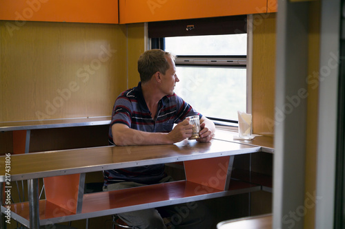 The man is sad at the window in the train car. A man in depression sits in a restaurant car and looks out the window.