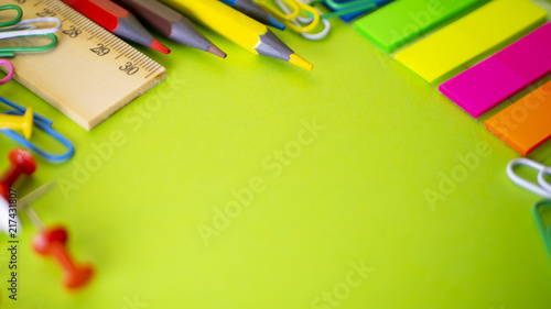 School supplies on green background with copy space. Pens, pencils, scissors, ruler, paper clips and marker on table at office