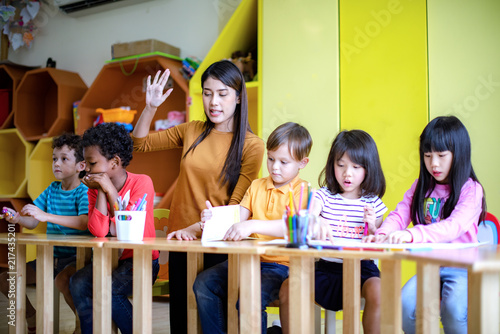woman teacher in classroom teaching preschool kids, joyful learning together with mixed-race international children