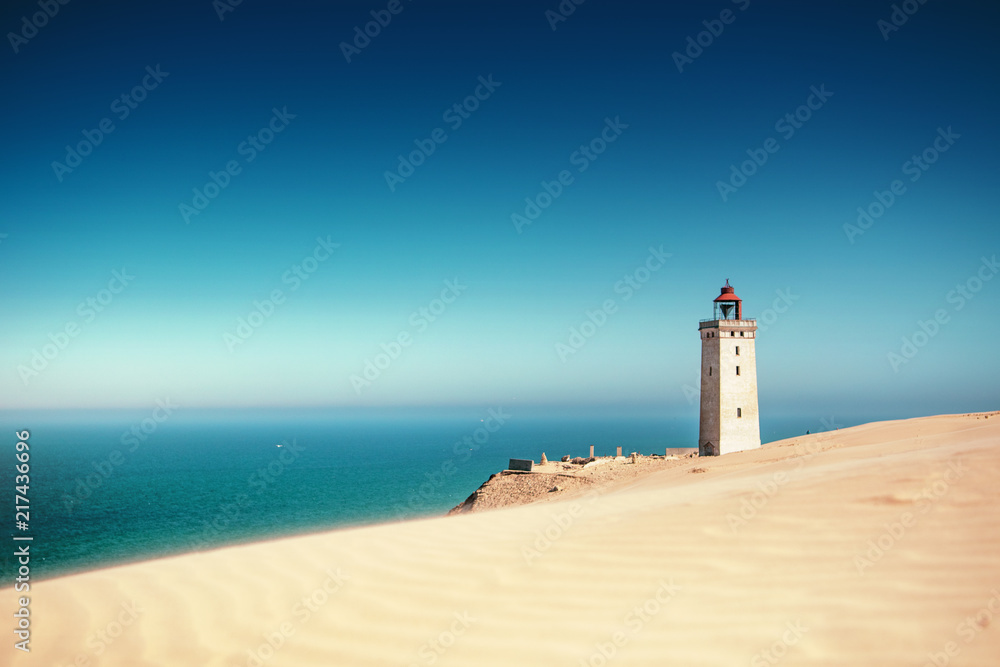 Bright beach sand dunes with the famous danish landmark lighthouse with blue sky background. Rubjerg Knude Lighthouse, Lønstrup in North Jutland in Denmark, Skagerrak, North Sea Bright beach sand dunes with the famous danish landmark lighthouse with blue sky background. Rubjerg Knude Lighthouse, Lønstrup in North Jutland in Denmark, Skagerrak, North Sea