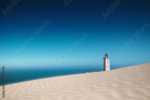 Bright beach sand dunes with the famous danish landmark lighthouse with blue sky background. Rubjerg Knude Lighthouse, Lønstrup in North Jutland in Denmark, Skagerrak, North Sea