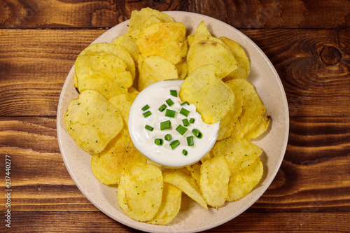 Crispy potato chips with green onion and sour cream on wooden table. Top view