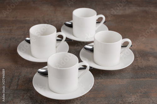 four white empty cups on saucers, four spoons, on a brown table, a concept of nutrition