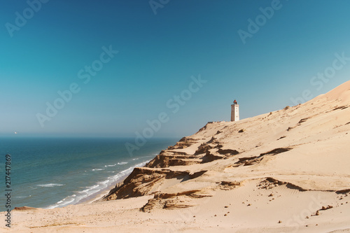 Bright beach sand dunes with the famous danish landmark lighthouse with blue sky background. Rubjerg Knude Lighthouse  L  nstrup in North Jutland in Denmark  Skagerrak  North Sea