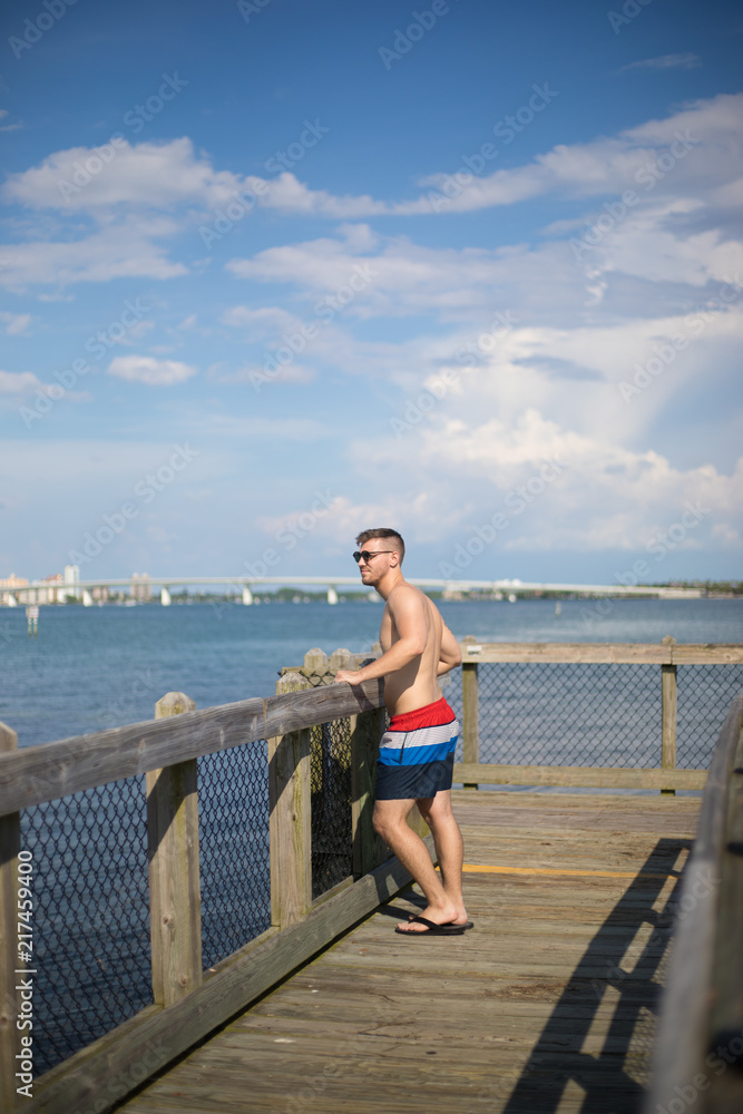 Young White Man Walking Down Florida Pier in Swim Trunks