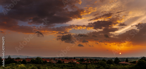 lever de soleil rouge au-dessus des collines avec un village en bas à gauche sous un ciel nuageux et dense