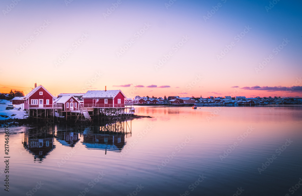 Famous tourist attraction of Reine in Lofoten, Norway with red rorbu houses water reflection at sunrise.