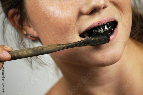 young woman brushing her teeth with a black tooth paste with active charcoal, and black tooth brush on white background for Teeth whitening © annebel146