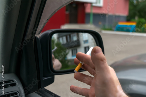 close-up of a cigarette in the hand of a man in the car, who watches the entrance door of the house