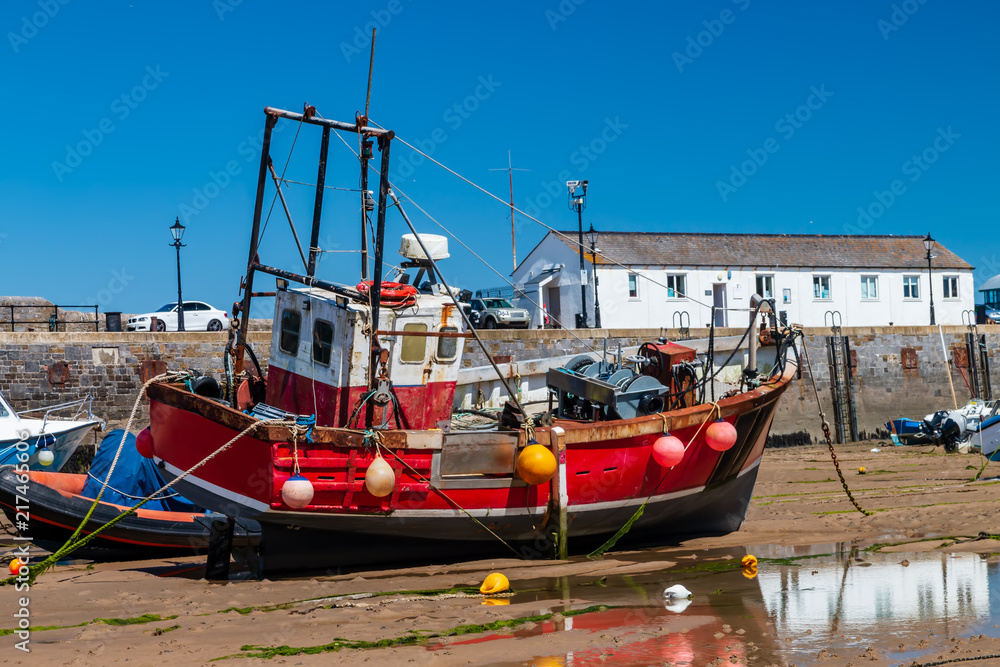 Colorful fishing and pleasure boats resting on the sand at a harbor during low tide on a sunny day
