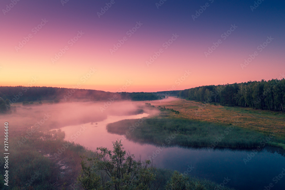 Aerial view of countryside and river in early misty morning. Trees along river. The time before sunrise. View from above