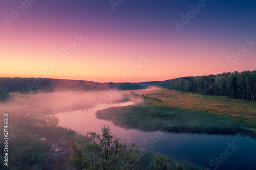 Aerial view of countryside and river in early misty morning. Trees along river. The time before sunrise. View from above