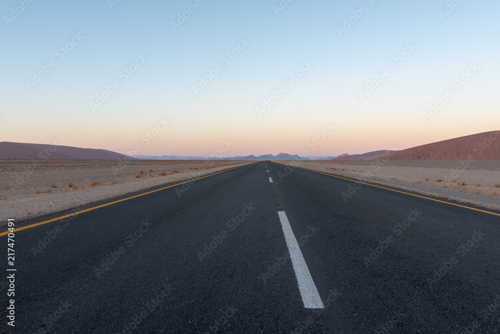 Straight road though desert dunes towards sunset mountains, Sossusvlei, Namib  desert, Naukluft National Park, Namibia