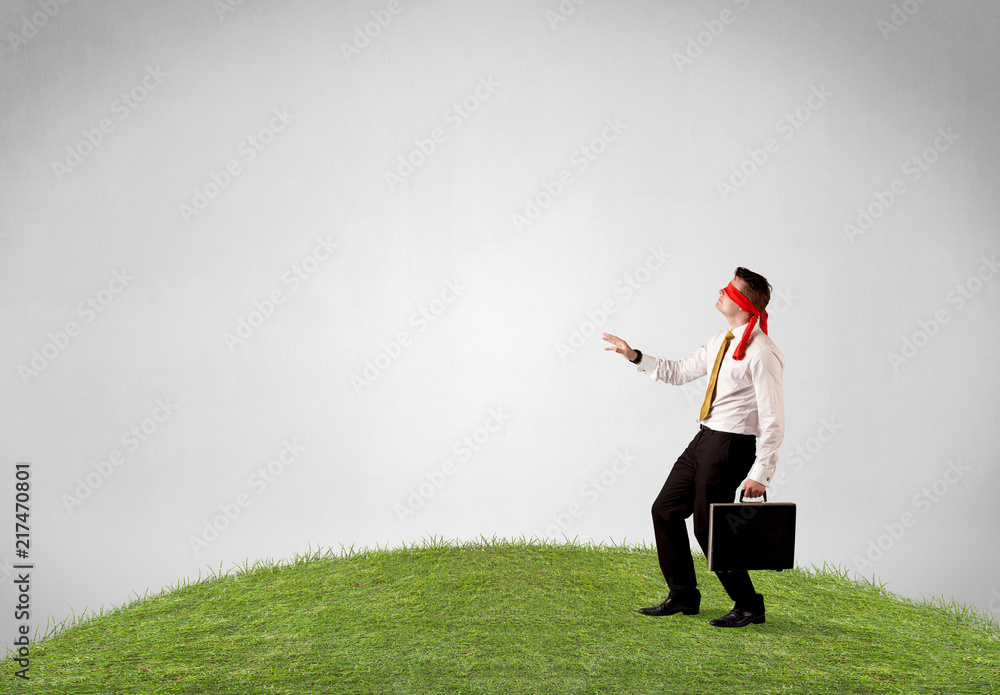 Young blindfolded businessman steps on a patch of grass Young blindfolded businessman steps on a patch of grass