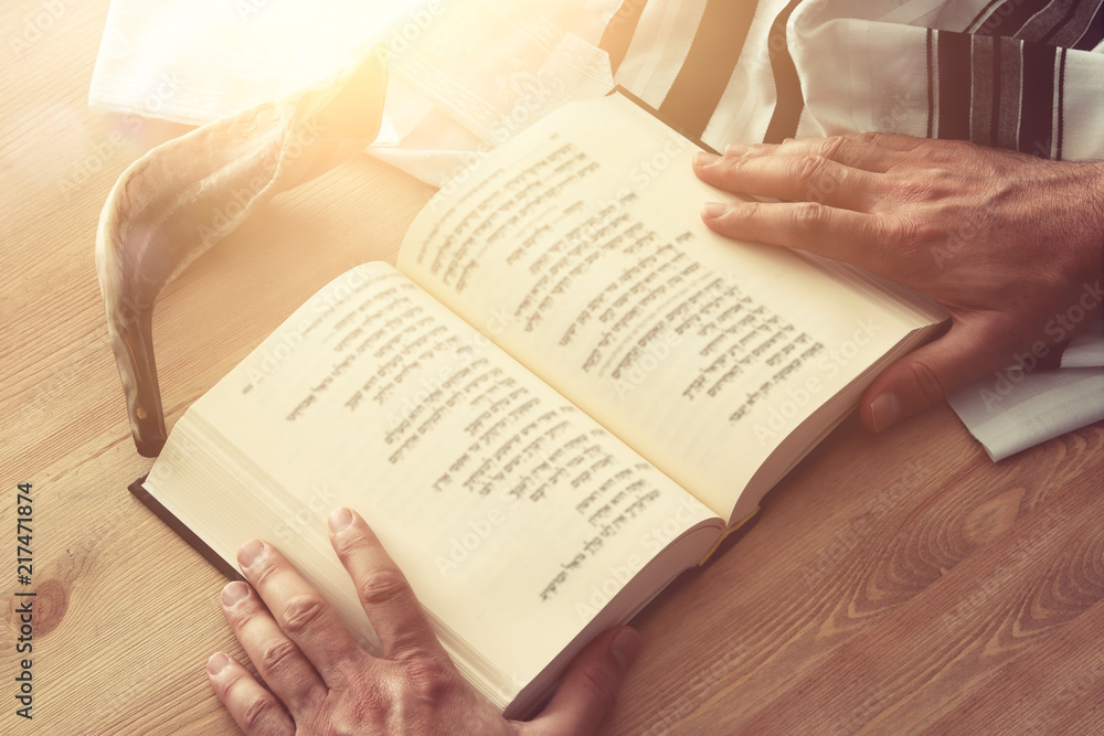 Naklejka premium Jewish man hands holding a Prayer book, praying, next to tallit. Jewish traditional symbols. Rosh hashanah (jewish New Year holiday), Shabbat and Yom kippur concept.
