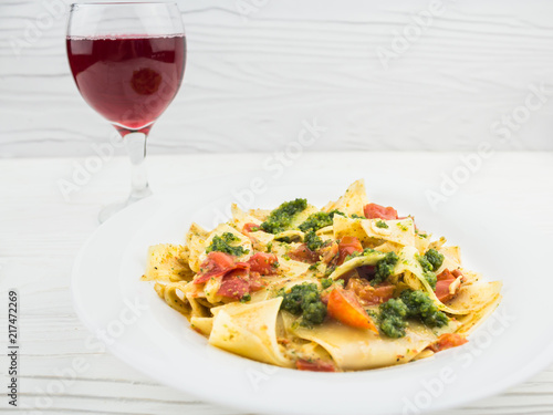Italian pasta with tomatoes and a glass of wine, on a wooden background