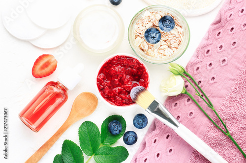 Natural skin care cosmetic products homemade with berries, oat flakes. Bowls of bright facial mask and scrub above with bathroom towel. 