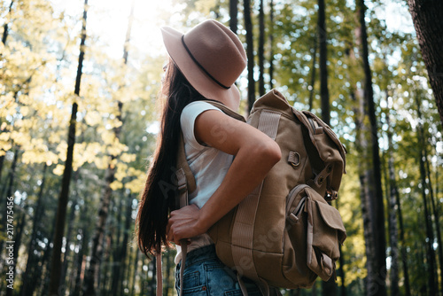 Traveler woman with backpack traveling among trees in forest. Young hipster girl walking on outdoors