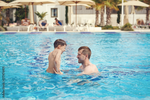 Father and son are having fun in the swimming pool at the hotel.