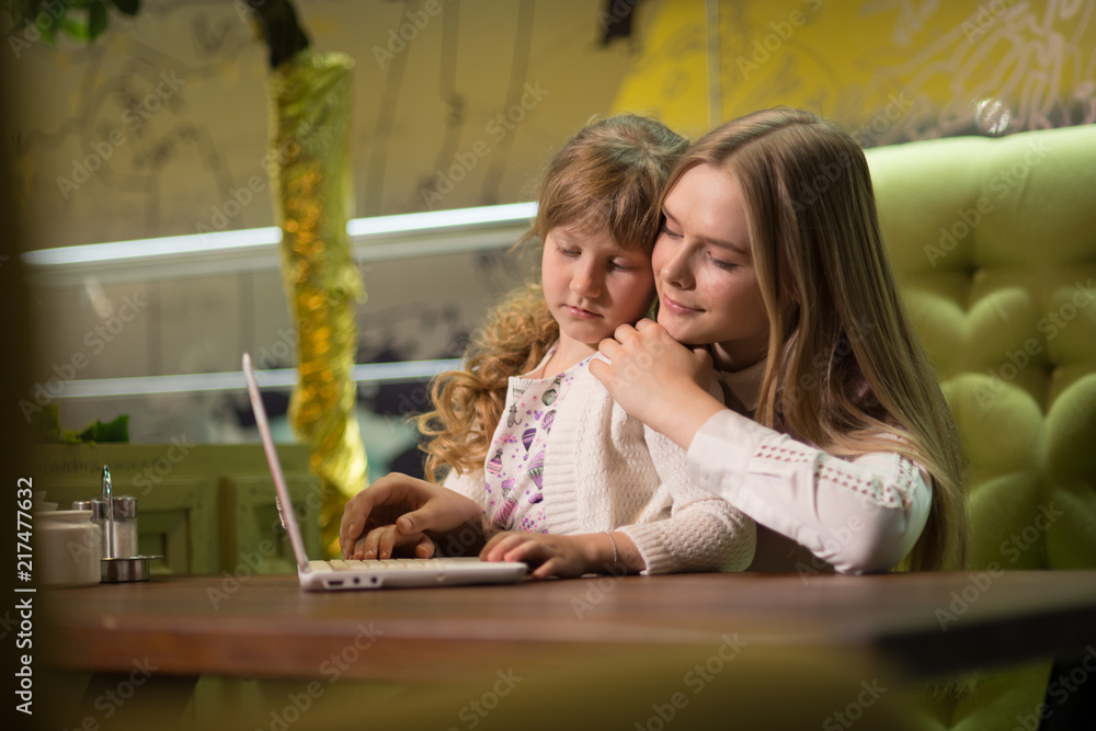 girl and little girl sitting at table with laptop girl and little girl sitting at table with laptop