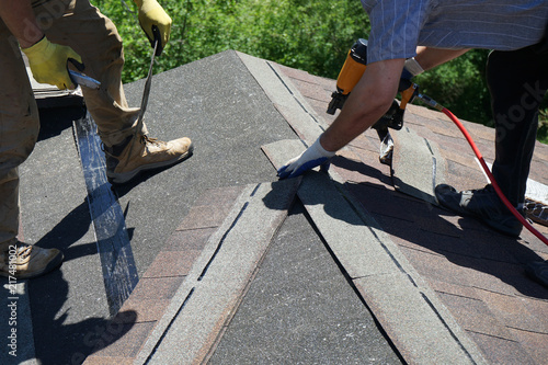 Roofer builders installing Asphalt Shingles or Bitumen Tiles on a roof of a new house.