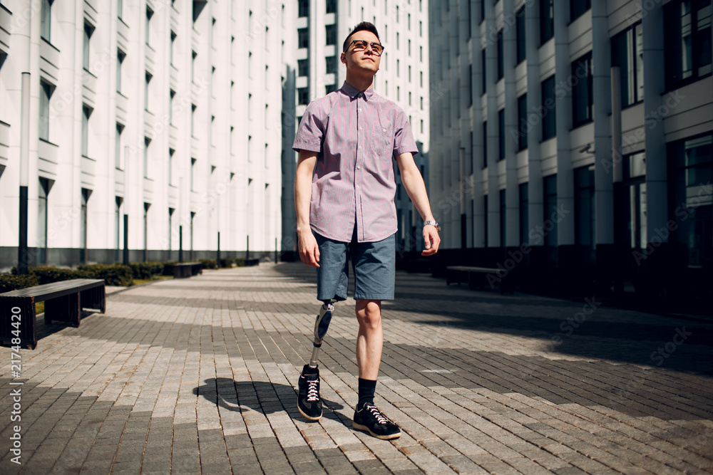 Disabled young man with foot prosthesis walks along the street.