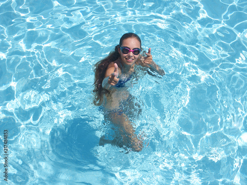 Cheerful girl in pool smiling and showing thumbs up