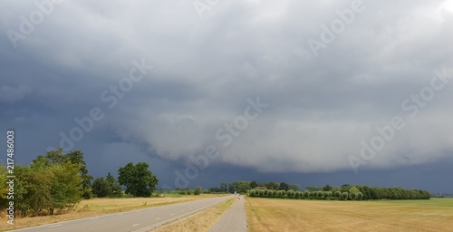 wall cloud of a thunderstorm above dry yellow fields and green trees in Laag Zuthem in Overijssel, the Netherlands
