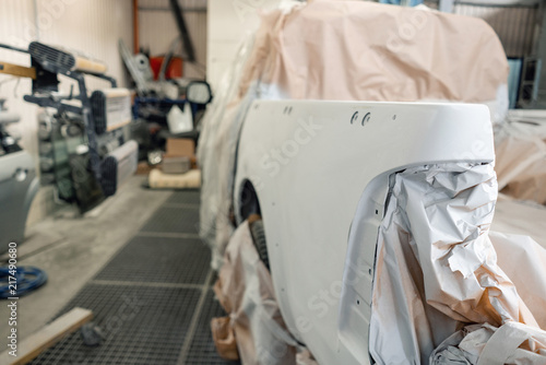 Garage painting car service. section of the car is covered with primer. vehicle is covered with protective paper. Repairing car body work after the accident by working sanding primer before painting.