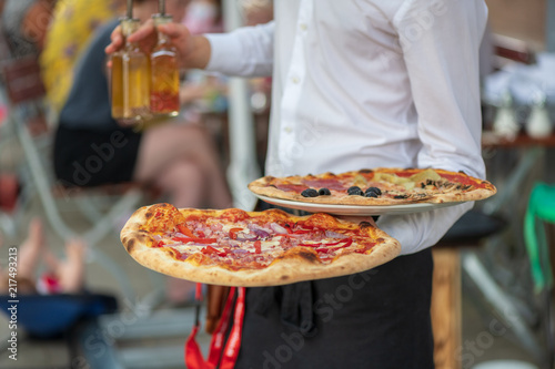 Italienischer Kellner bedient auf der Terrasse  mit zwei Pizza in der Hand  photo