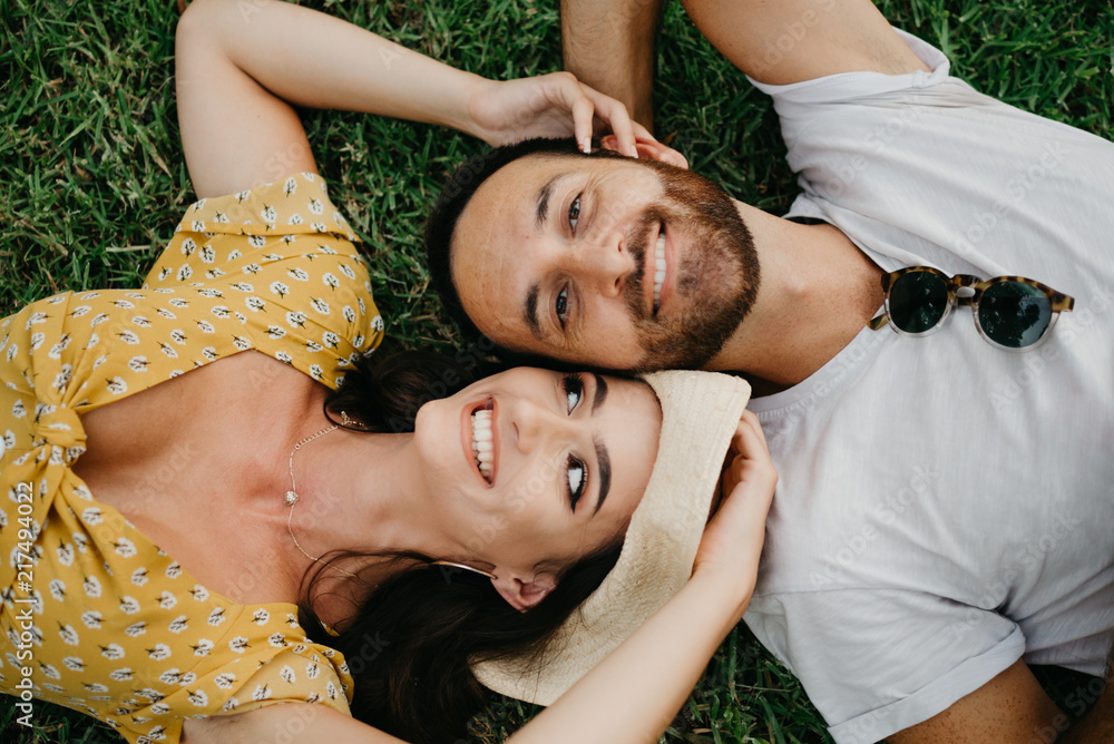 Stylish pretty brunette girl with her boyfriend with beard with smile lying close to each other on the grass in Spain in the evening.