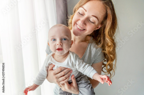 Young mother holding newborn child. Woman and infant boy relax and playing in bedroom near windiow. Mom of breast feeding baby. Family, maternity, tenderness, parenthood, responsibility concept