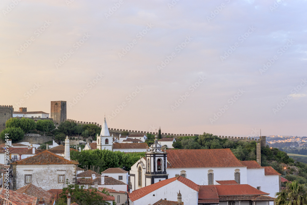 Scenic view of white houses red tiled roofs. and castle of Obidos from wall of fortress. Beautiful old town with medieval architecture in the sunset. Scenic view of white houses red tiled roofs. and castle of Obidos from wall of fortress. Beautiful old town with medieval architecture in the sunset.