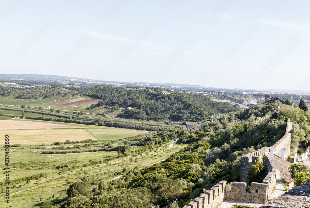 Scenic view of the valley and wall of fortress. White houses red tiled roofs Beautiful old town with medieval. Obidos village, Portugal. Summer sunny day.