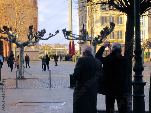two old tourists stop at attraction in Dusseldorf, Germany in December while one takes a picture