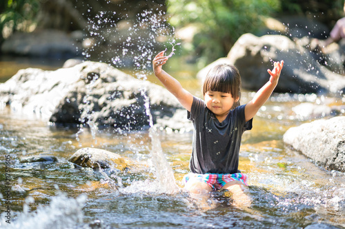 little asian girl playing in waterfall stream with water splash