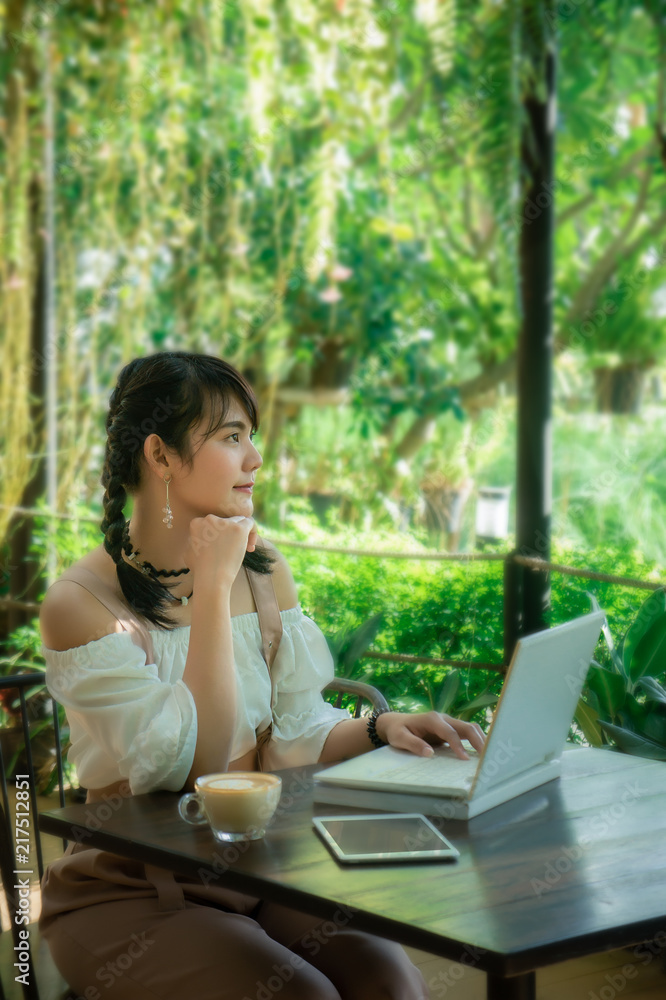 asian girl's sitting and using laptop looking smile on work in the cafe asian girl's sitting and using laptop looking smile on work in the cafe