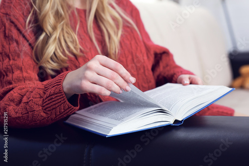 Middle section of young woman reading book at home interior background