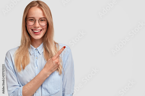 Happy lovely young female with gentle smile, red manicure, points aside at up...