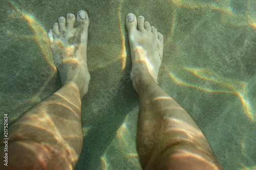 Pair of male feet on sun lit sand sea bottom, view from above, underwater photo. © Lubo Ivanko