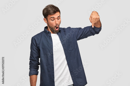 фотографія Photo of surprised unshaven young male points down with impressed expression, op