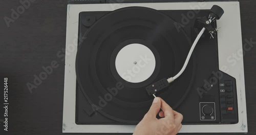 The man's hand puts the needle on the vinyl record and starts the player. photo