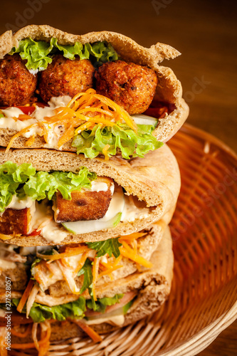 Concept of vegetarian food. pita with falafel, salad, vegetables, tofu cheese in a wicker basket on a wooden table. background image. Copy space, selective focus
