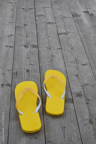 Yellow flip flops on grey natural weathered wooden background with copy space for text. Summertime leisure concept.
