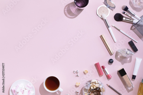 Makeup products and coffee or tea cup on pink color background with hard light and shadows, flat lay and top view