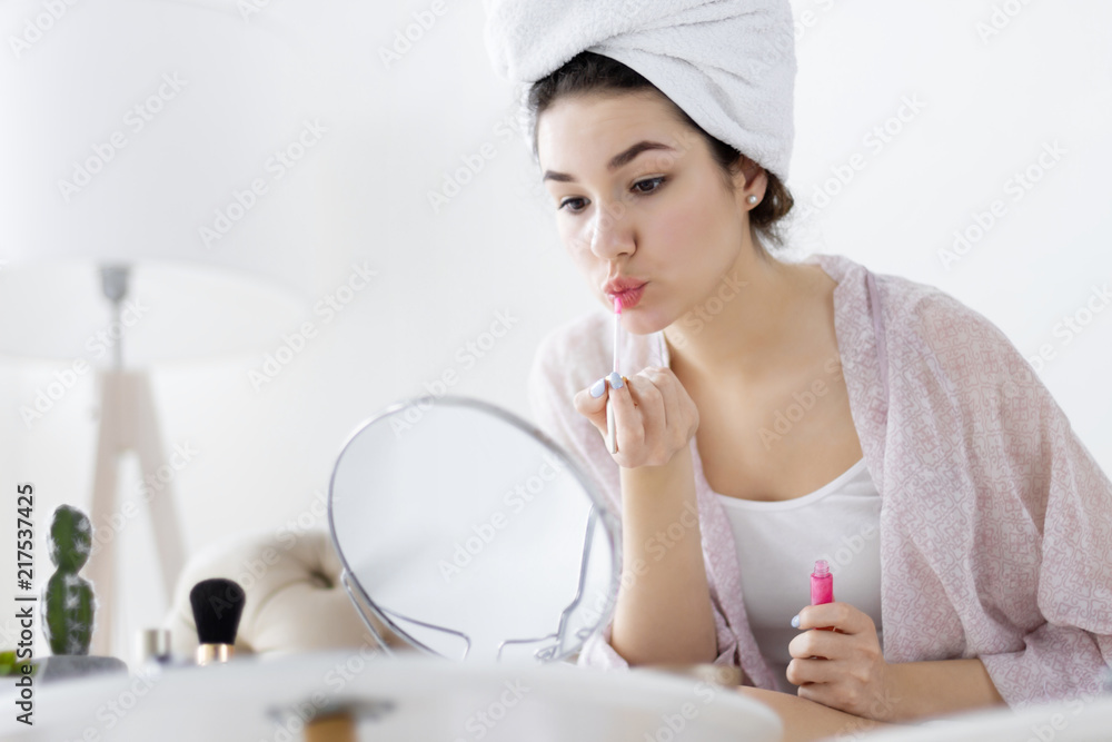 Young girl female woman after shower wearing white underwear and white towel sitting on sofa and doing make up / painting lips with lipstick in front of mirror in light room. Preparing for day concept Young girl female woman after shower wearing white underwear and white towel sitting on sofa and doing make up / painting lips with lipstick in front of mirror in light room. Preparing for day concept